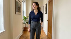 Adult woman with an authentic hourglass silhouette standing in a sunlit interior wearing tailored high-rise trousers and tucked knit top